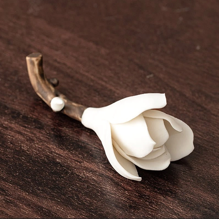 Close-up top view of handcrafted ceramic magnolia ornament with pure white flower petals and brown branch accent on dark wood