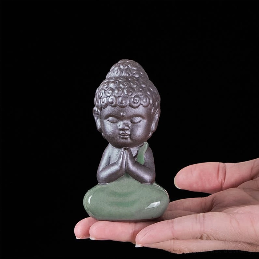 Small handcrafted ceramic meditation monk statue held in palm showing miniature size