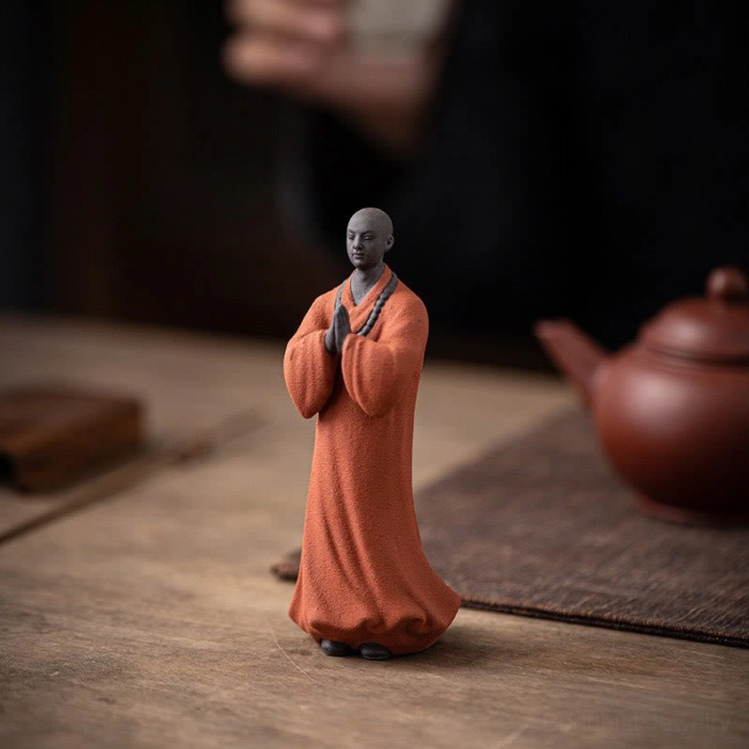 Handcrafted ceramic Buddhist monk statue displayed on tea table with decorative accessories and natural lighting