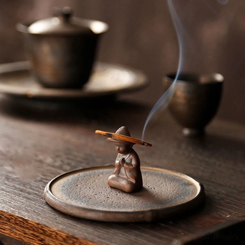 Vintage brown ceramic monk incense burner with burning incense on traditional tea table with gaiwan tea set