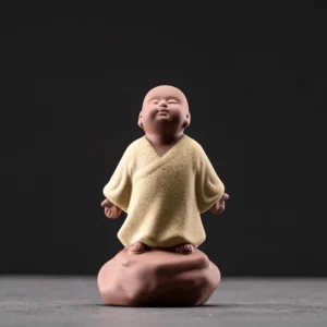 Beige ceramic looking up monk statue in meditative pose on brown stone base, studio front view