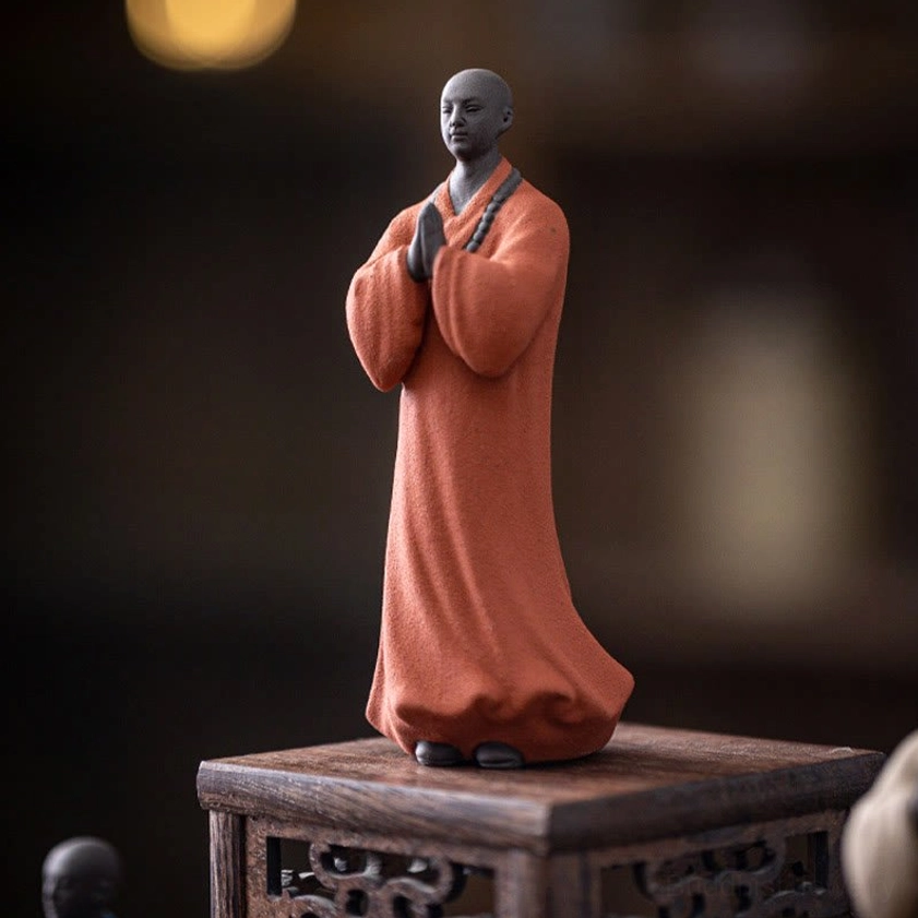 Ceramic meditation monk figurine with terracotta matte robe displayed on carved wooden pedestal