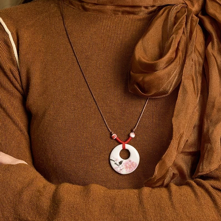 Buddhist ceramic pendant necklace close-up handheld worn styling on brown fabric background