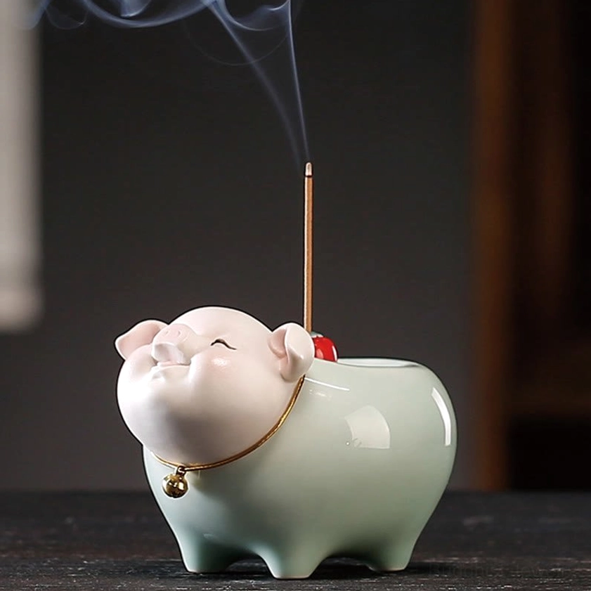 Close-up front detail of ceramic pig incense burner face, gold bell collar and facial features against plain dark backdrop