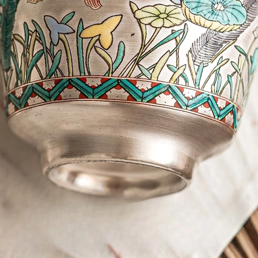 Close-up detail of ceramic tea cup base with geometric trim and silver polish, grass-flower patterns