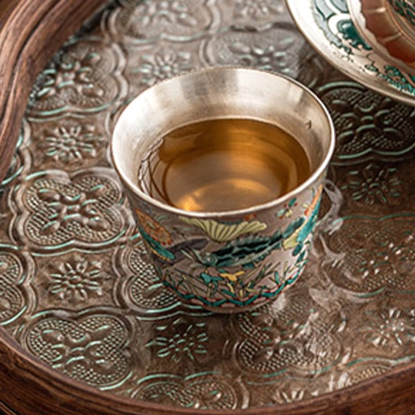 Brewed tea in handcrafted ceramic cup with fish motif, silver interior on serving tray