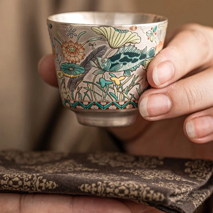 Ceramic gongfu tea cup held in hand, showing fish and lotus floral patterns, side profile