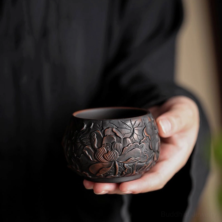 Dark matte ceramic kung fu tea cup with embossed floral details held in hand during tea ceremony