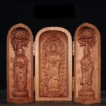 Front view of tri-fold cherry wood Buddhist altar shrine with gilded hinges displaying three carved Buddha statues on dark wood table