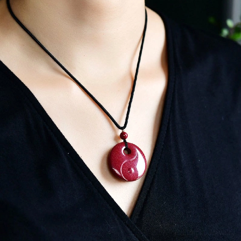 Chinese zodiac cinnabar Buddhist necklace pendant held in fingers showing deep red granular texture and zodiac carving