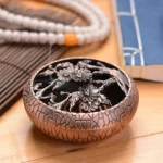 Chrysanthemum carved brass incense burner with hollow lid design, displayed on wooden meditation table with prayer beads and Buddhist books, copper red crackle finish