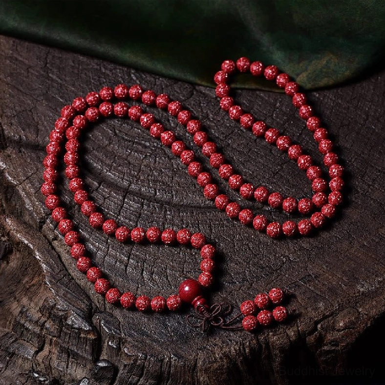 Coiled cinnabar 108-bead mala prayer beads necklace on dark wood with green fabric backdrop