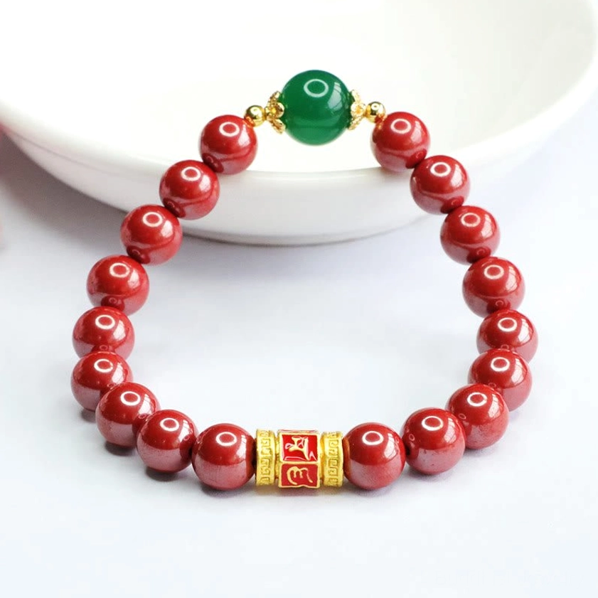 Sacred Buddhist blessing bracelet with red cinnabar beads, green stone, and engraved gold mantra barrel bead overhead view