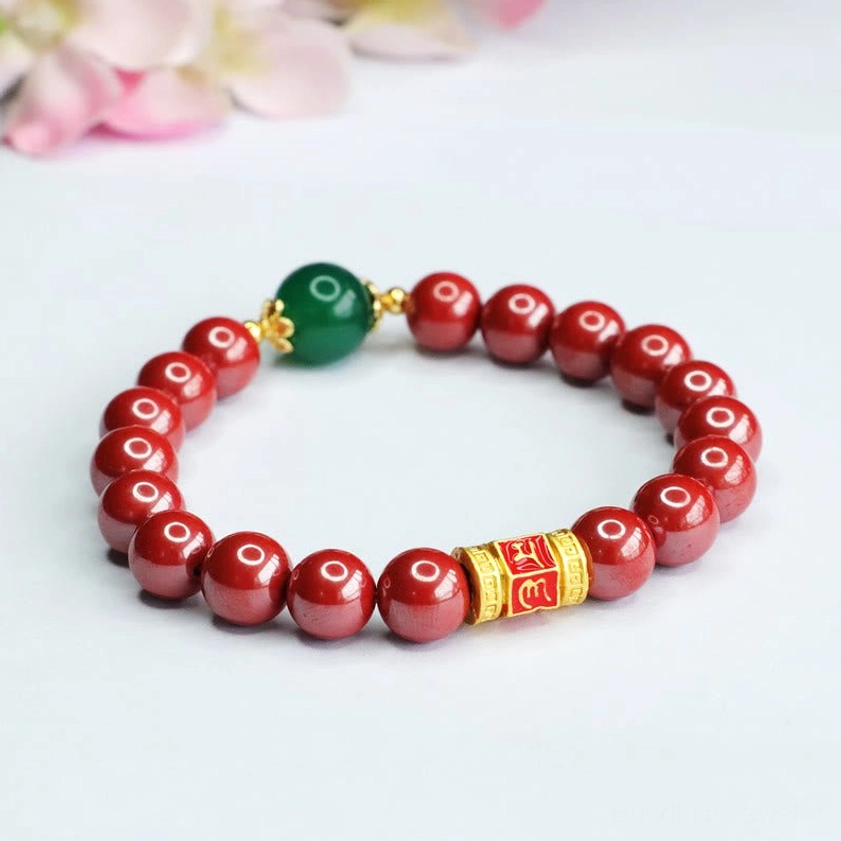 Handmade cinnabar and green agate Buddhist bracelet with gold engraved mantra beads on nature background