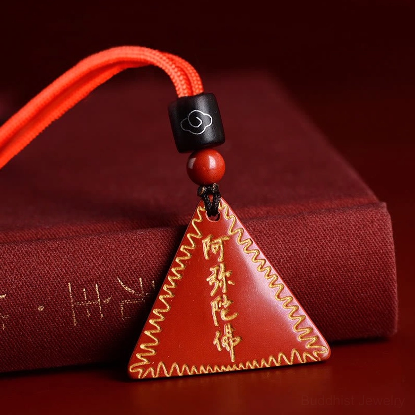 Orange-red cinnabar Amitabha pendant with braided orange cord displayed on red fabric box