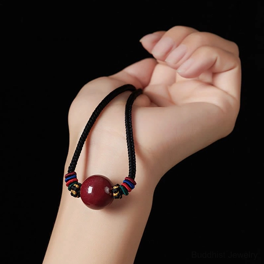 Overhead view of handmade cinnabar bead Buddhist pendant - single red bead with colorful woven knots and black cord