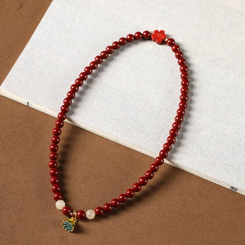 Long cinnabar rosary bead strand with enamel lotus pendant and accent beads on brown linen background