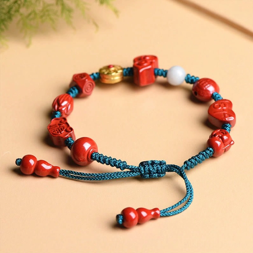 Circular overhead view of red cinnabar blessing bracelet with adjustable gourd-shaped tassel ends and white gold accents