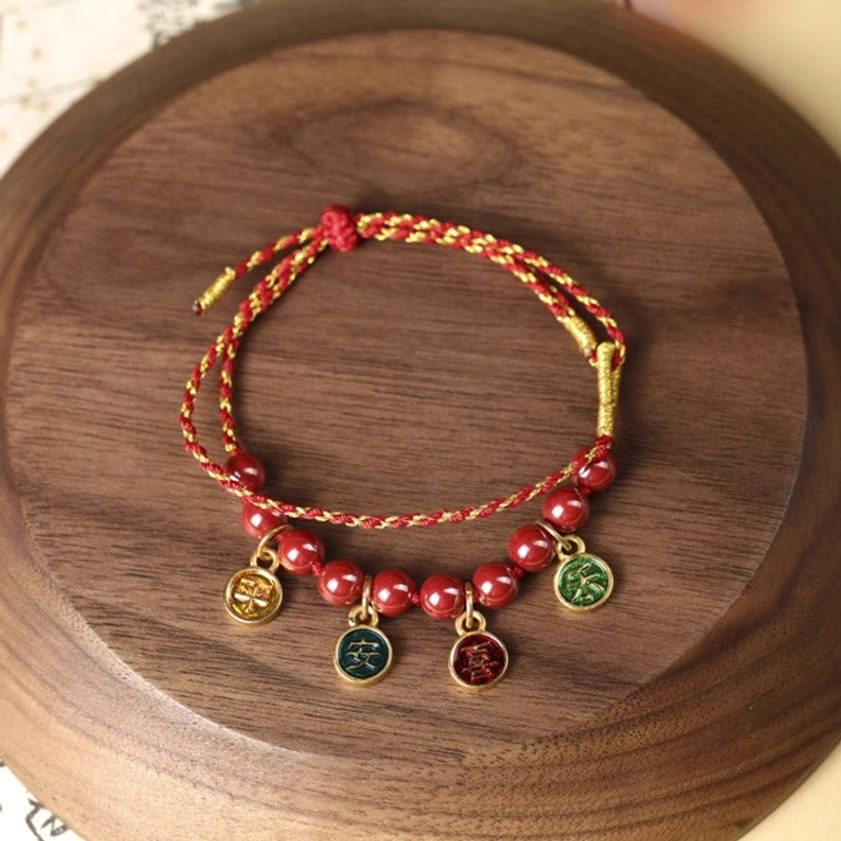 Handcrafted cinnabar bracelet flat lay, showing intricate woven red string and natural stone beads with metal charms