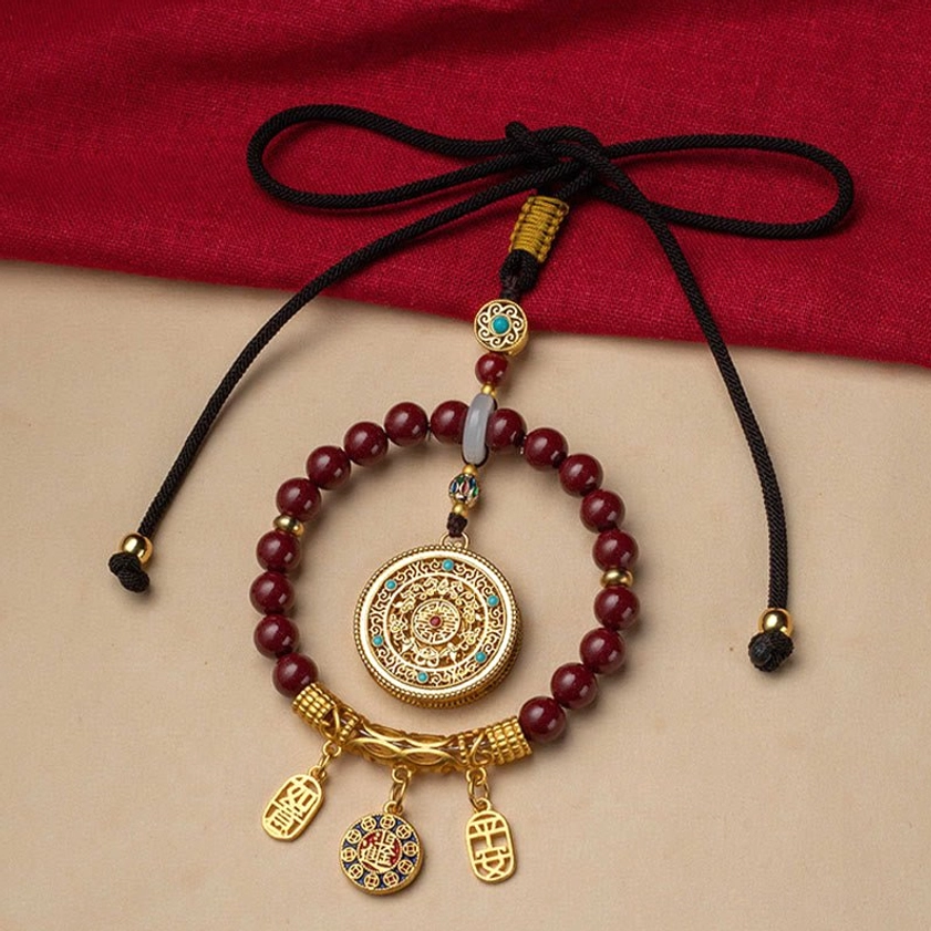 Cinnabar Buddhist blessing car hanging decoration with braided black cord and adjustable knot on red backdrop, handcrafted artisan piece