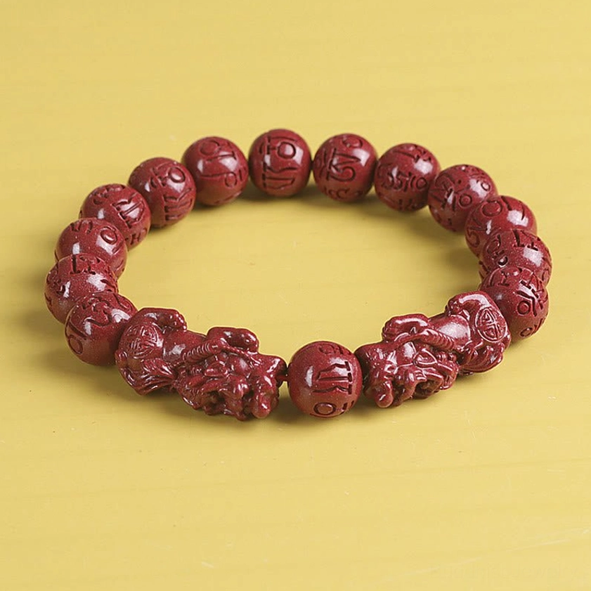 High-angle view of red cinnabar bracelet with single large engraved bead and Pixiu charms