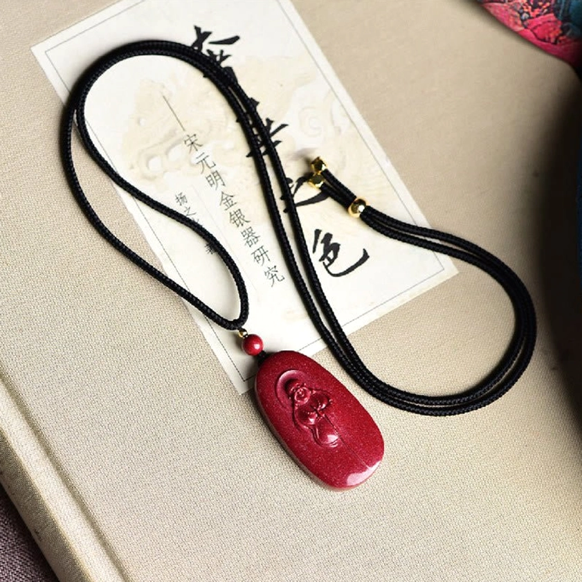 Complete cinnabar laughing Buddha Buddhist necklace on black braided cord displayed on antique book page, full-length view