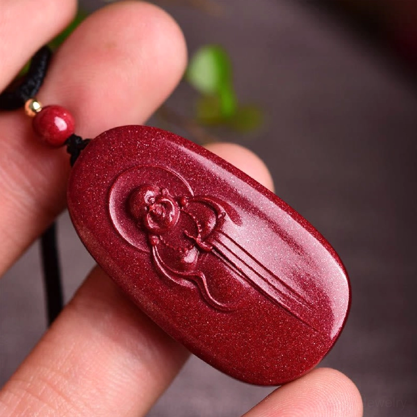 Cinnabar laughing Buddha Buddhist necklace pendant held in hand showing deep red shiny granular texture and carving details