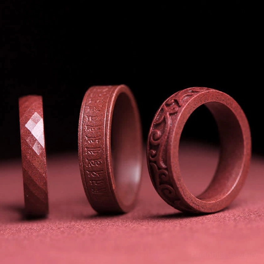 Three handcrafted cinnabar Buddhist blessing rings featuring Om Mani Padme Hum mantra carving, faceted design, and auspicious clouds motif on wine-red fabric background