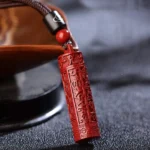 Red cinnabar Buddhist mantra pendant necklace with carved scriptures, displayed on dark wooden tray with accent beads, three-quarter close-up view