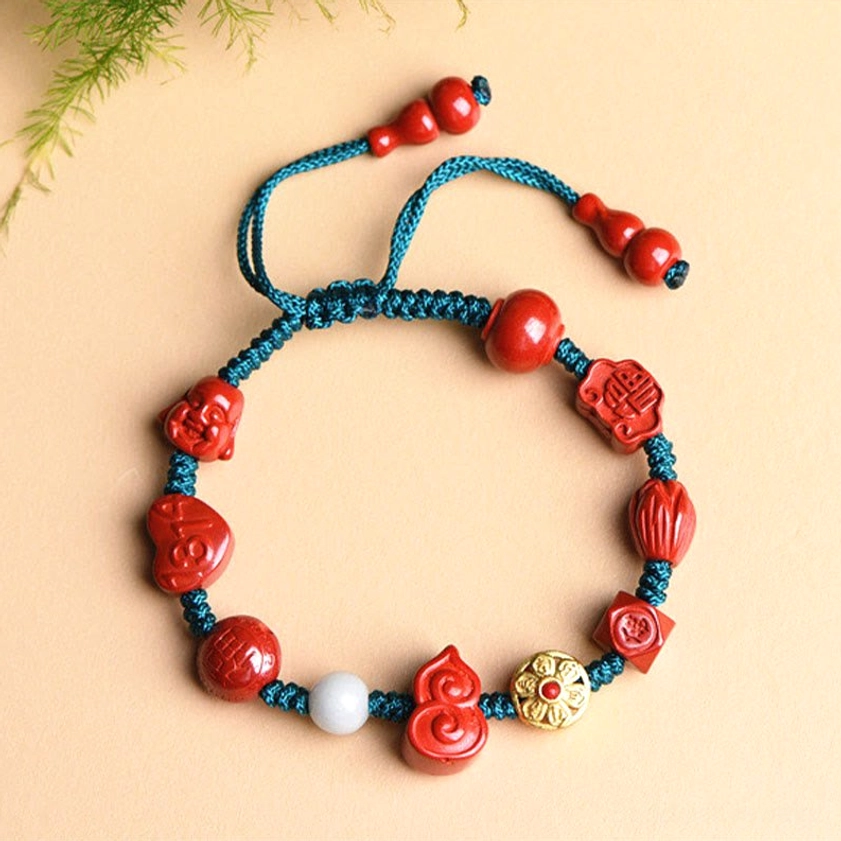 Top-down flat lay view of natural cinnabar prayer bracelet showing carved Buddhist emblem beads, white accent bead, and gold-tone charm