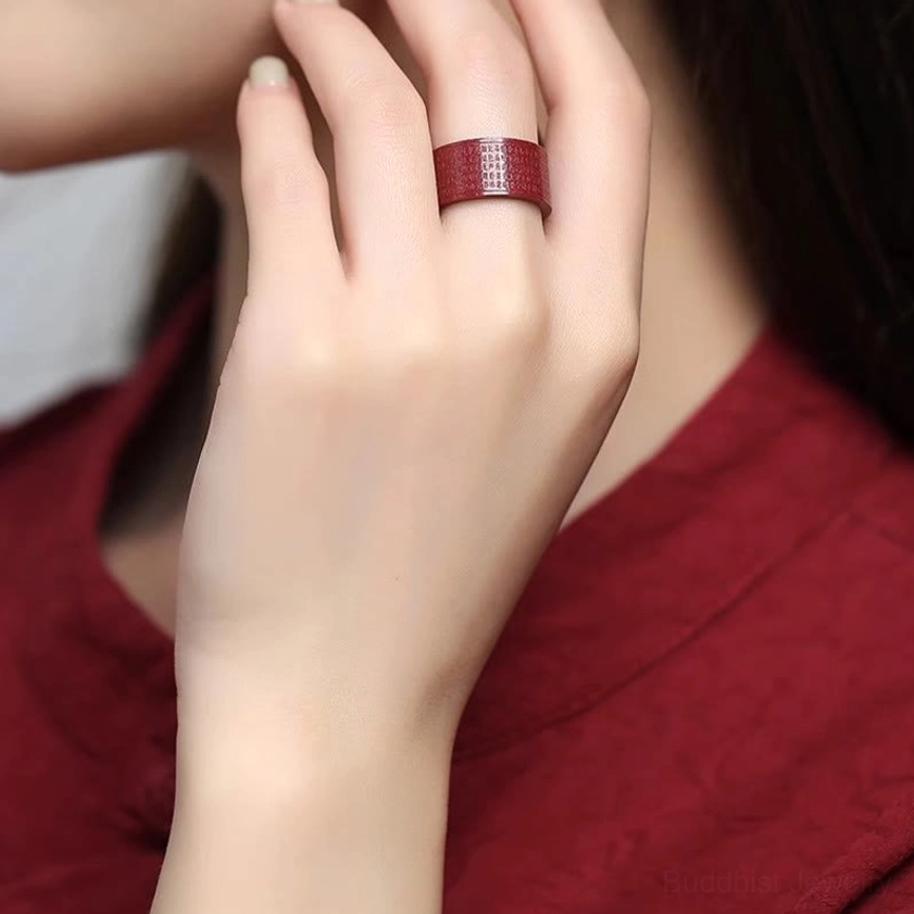 Woman wearing cinnabar engraved Buddhist mantra ring on middle finger close-up hand shot with red clothing