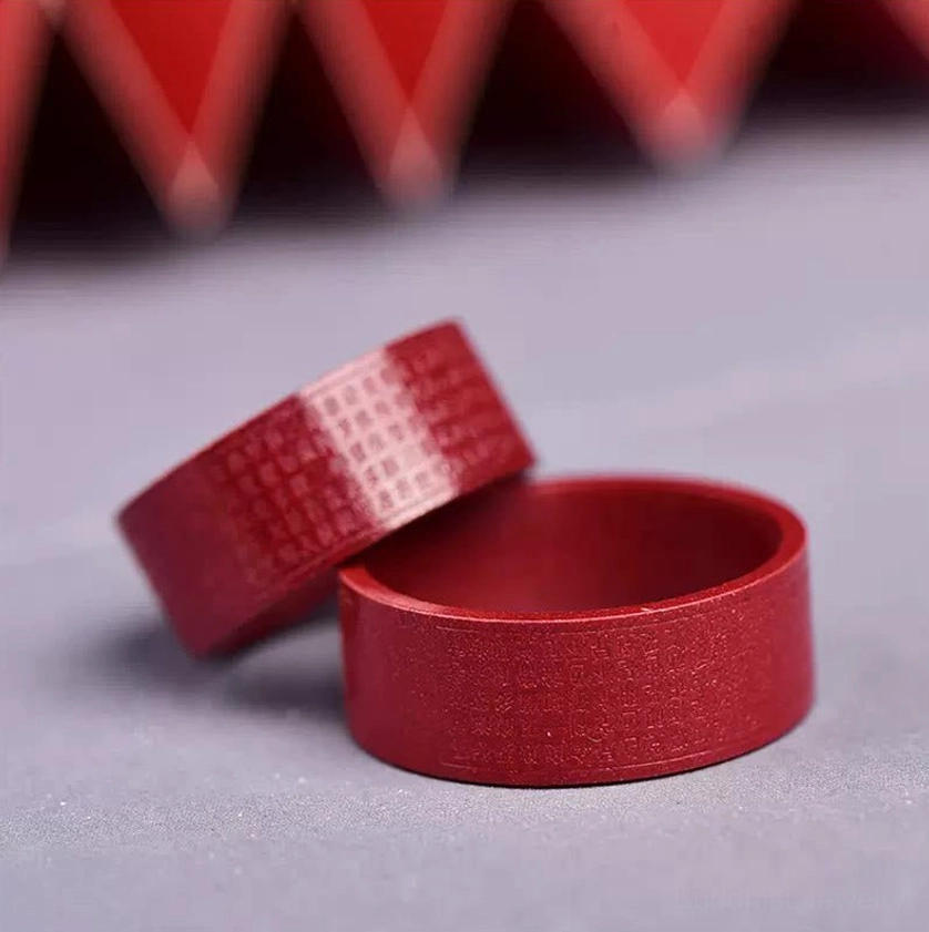 Two cinnabar Buddhist rings overhead view one engraved one smooth on light gray background with red decor