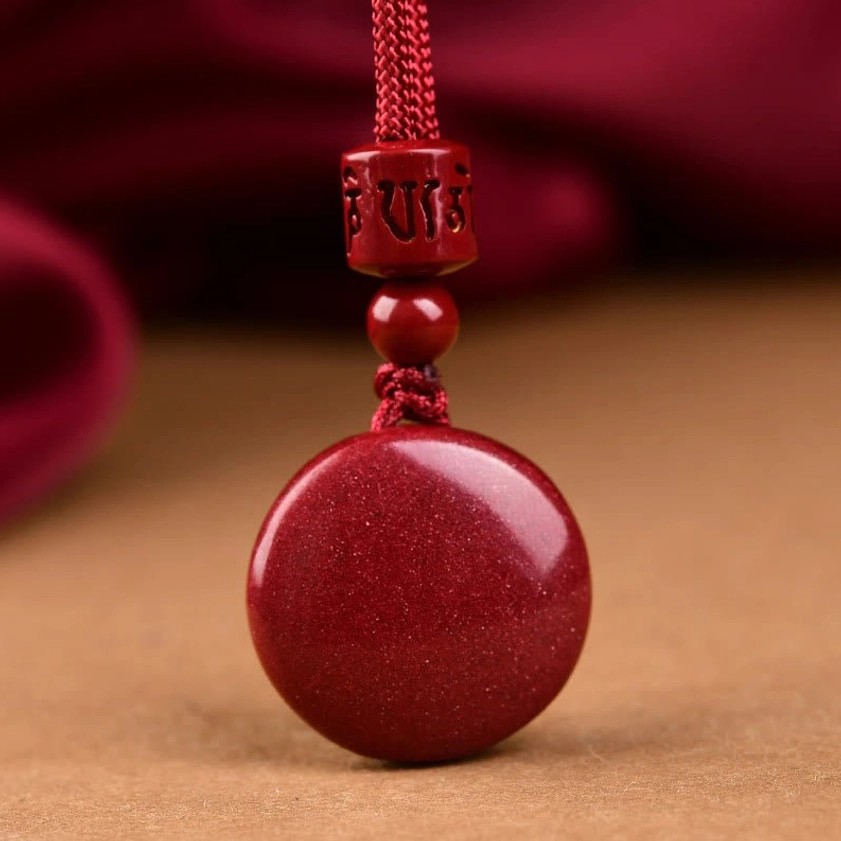 Plain carved cinnabar round pendant with Six True Words mantra on red braided silk cord