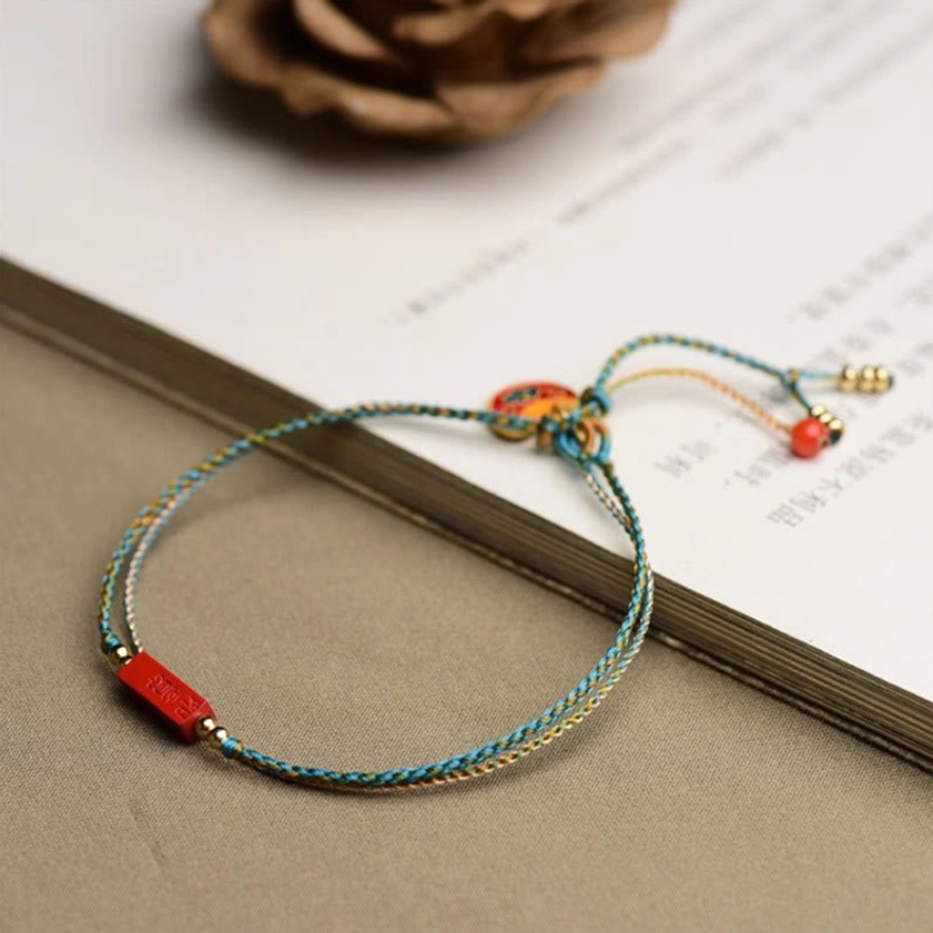 Minimalist handmade cinnabar bracelet with cloud enamel charm and red bead tassel on paper book surface