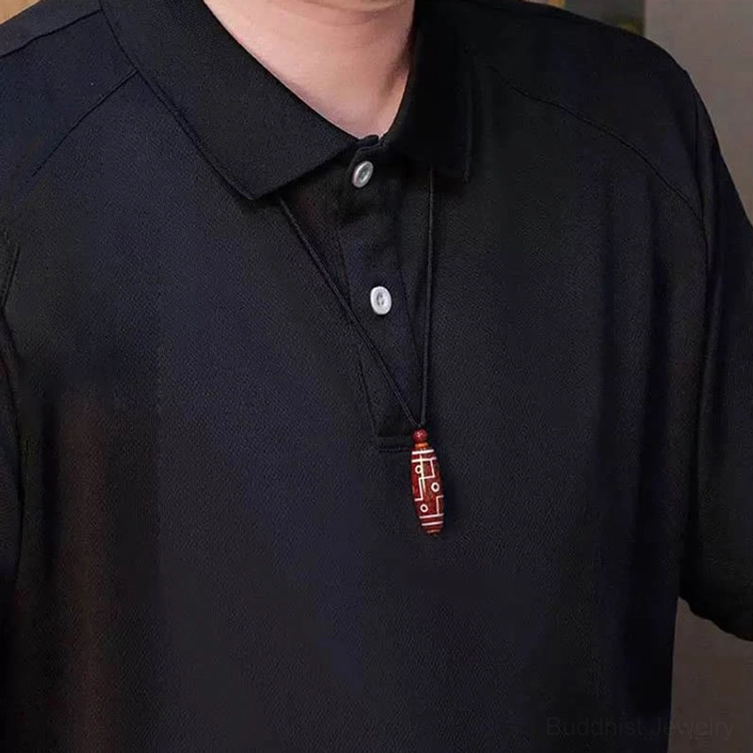 Man wearing cinnabar dzi bead necklace pendant at chest level with black polo shirt, demonstrating daily wear styling for Buddhist protection jewelry