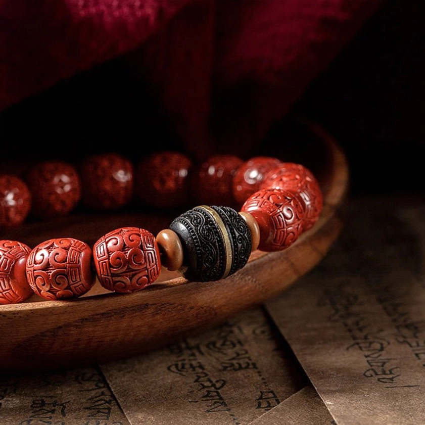 Close-up detailed view of cinnabar and ebony Buddhist blessing bracelet beads with metal-accented spacer on wooden bowl and red fabric backdrop