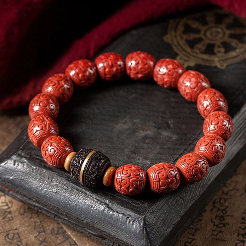 Cinnabar and ebony Buddhist bracelet flat lay on dark wooden tray with red fabric, showcasing detailed carved bead patterns and central spacer design