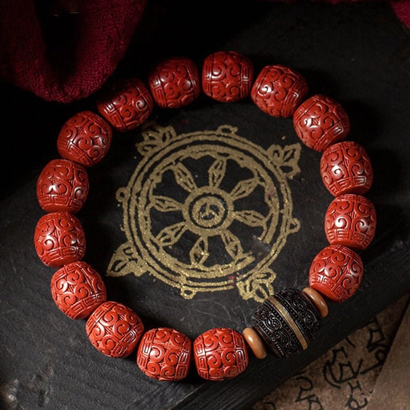 Cinnabar ebony Buddhist blessing bracelet displayed on Tibetan mandala mat with sacred scripture, overhead view showing hand-carved red beads and gold-accented ebony spacers