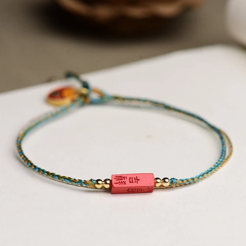 Enamel charm woven cinnabar bracelet with lock pendant and Ji Xiang blessing symbol on light desktop backdrop