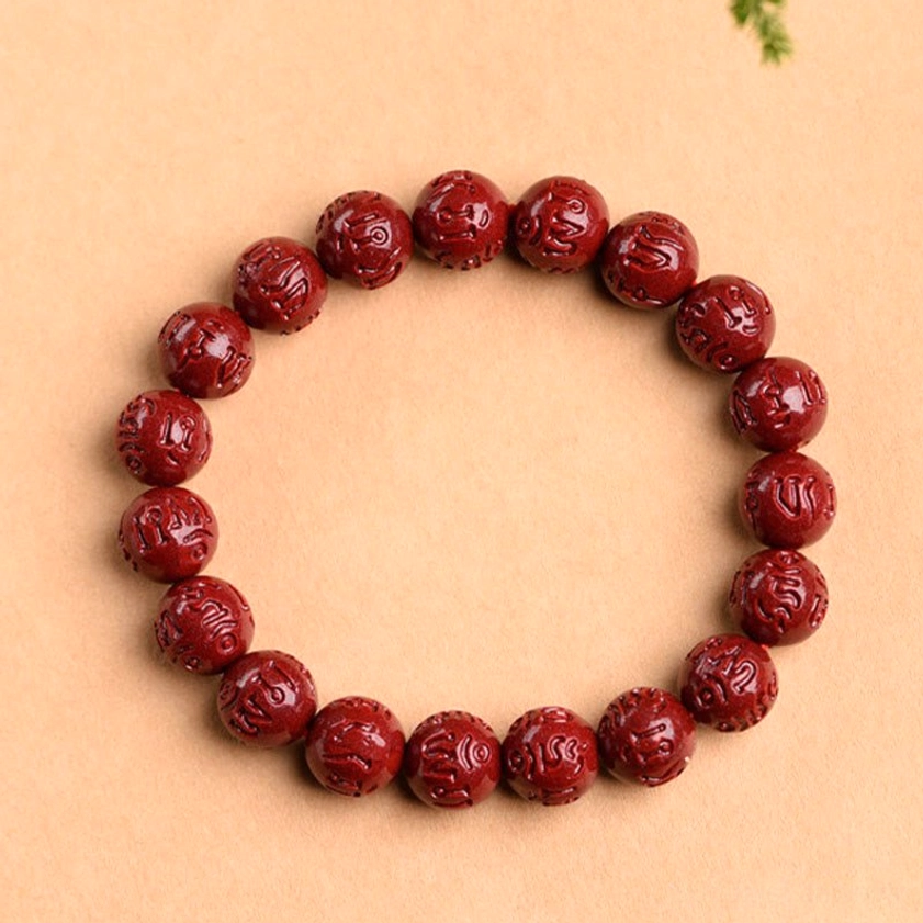 Natural cinnabar fret pattern bracelet displayed with green botanical accents on light background, showing carved bead details