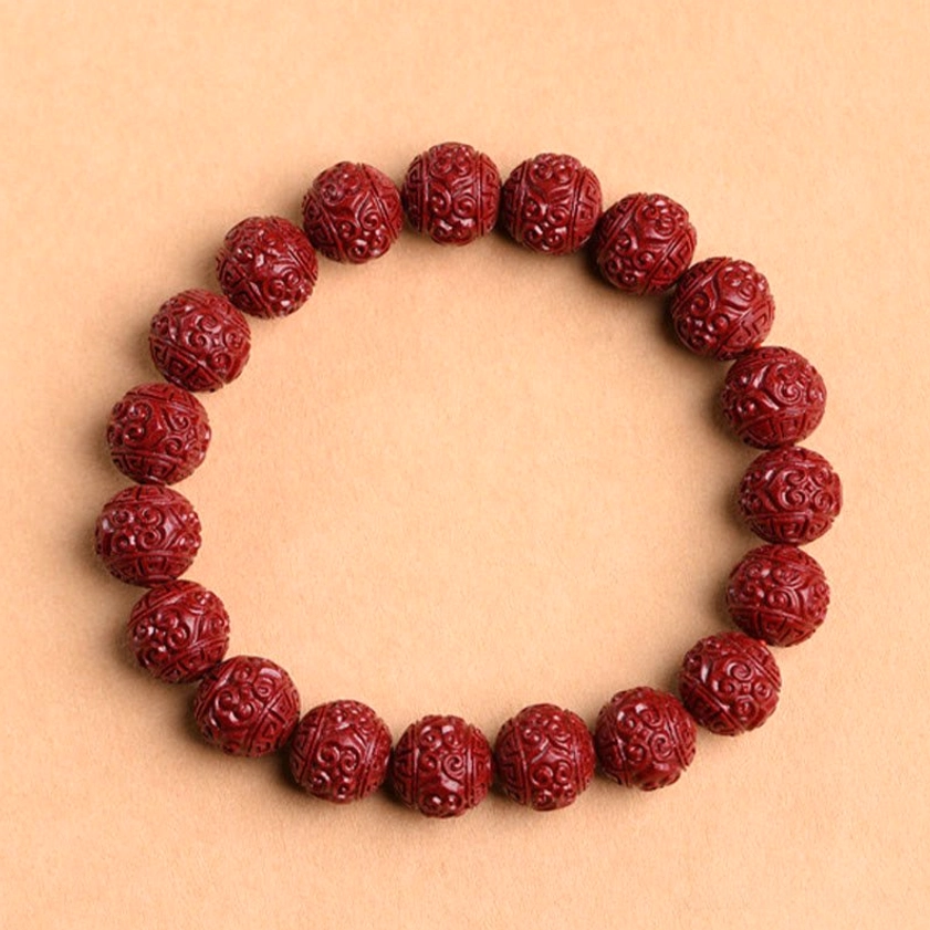 Handcrafted cinnabar prayer bracelet with fret pattern carvings showing deep red beads on elastic cord, full bracelet display