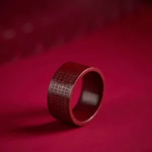 Cinnabar Buddhist mantra ring with engraved Heart Sutra, deep red matte finish, three-quarter side view on dark fabric background
