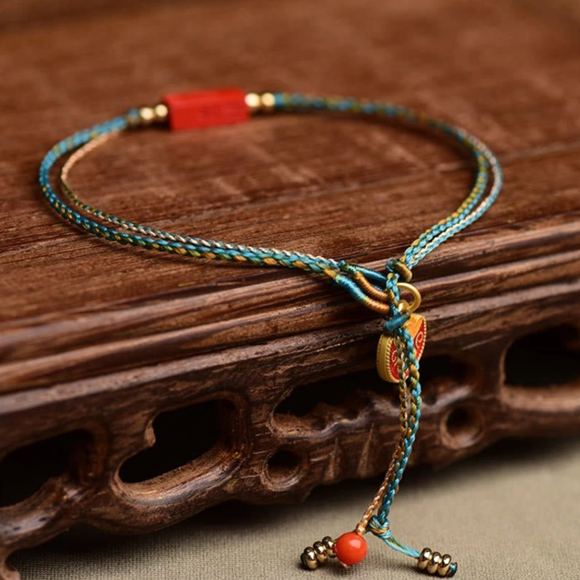 Close-up top view of cinnabar Buddhist bracelet showing rectangular Ji Xiang auspicious pendant and metal bead tassel with red accent