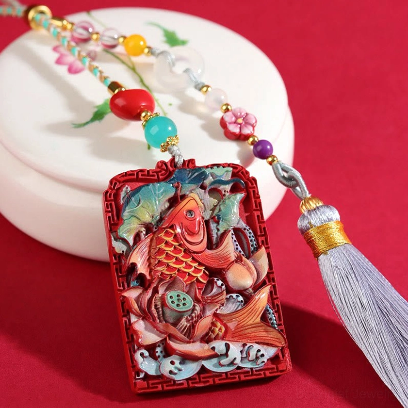 Cinnabar koi lotus blessing pendant with beaded hanging cord, displayed with decorative porcelain box and grey tassel on red backdrop