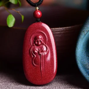 Handcrafted cinnabar laughing Buddha Buddhist necklace pendant with embossed Buddha carving on wine-red stone, displayed on ceramic tabletop with green foliage