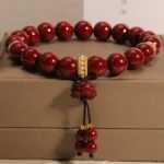 Cinnabar lotus blessing bracelet with deep red beads and gold crystal spacer, resting on luxury brown jewelry box with lotus charm pendant