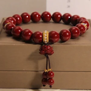 Cinnabar lotus blessing bracelet with deep red beads and gold crystal spacer, resting on luxury brown jewelry box with lotus charm pendant