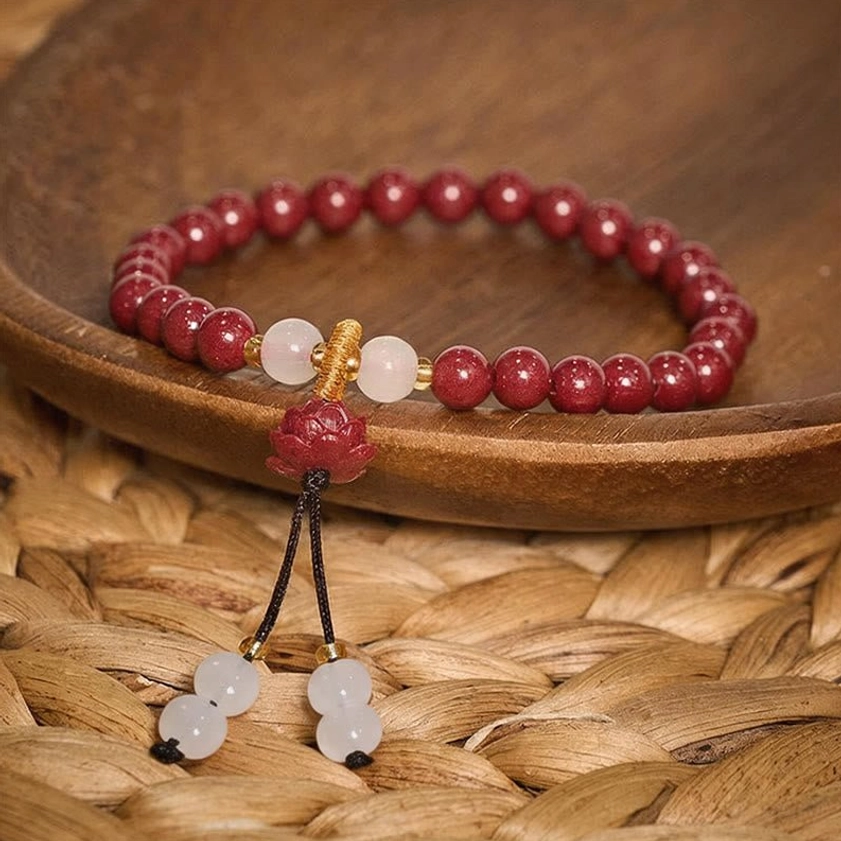 Close-up detail of cinnabar lotus bracelet with pendant charm and tassel on wooden bowl showing intricate Buddhist craftsmanship