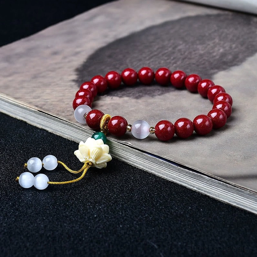 Cinnabar lotus blessing bracelet flat lay overhead view showing deep red beads, white spacers, carved off-white lotus charm, and golden tassel details