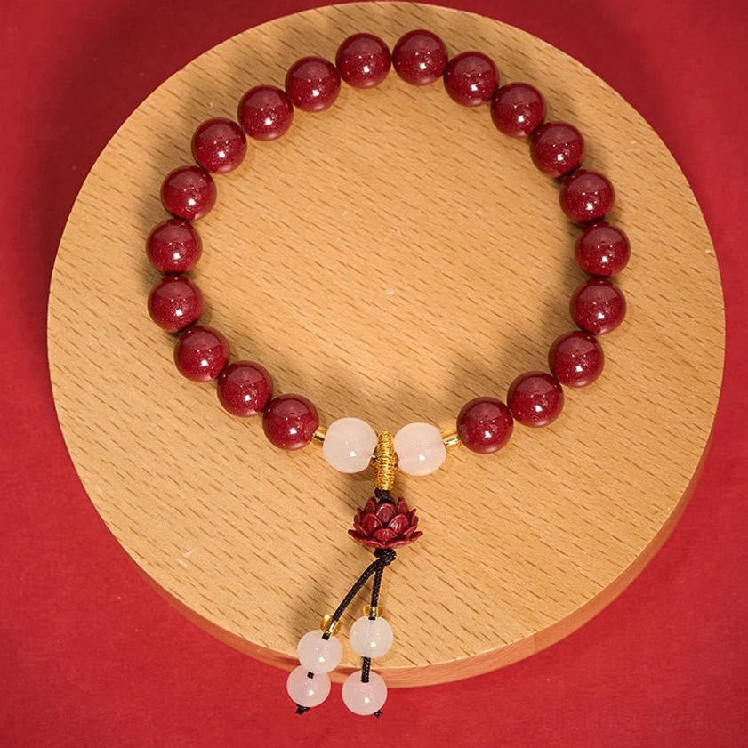 Full view cinnabar lotus bracelet displayed overhead on wooden plate showing complete beaded loop and spiritual pendant design